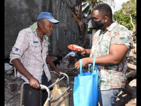 Pastor Junior White (right) gives a care package to Tyrone Phillips (left), an elderly man who lives in Allman Town, Kingston, yesterday. Phillips has to use a walker to move around was not sure where his next meal would be coming from.