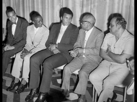 Muhammad Ali (centre) listens intently to Muslim Minister Jam Muhammad (in glasses) in the lobby of The Jamaica Pegasus hotel shortly before the start of reception for him on December 28, 1974. Others in picture from left are Louis Farrakhan, another Musli