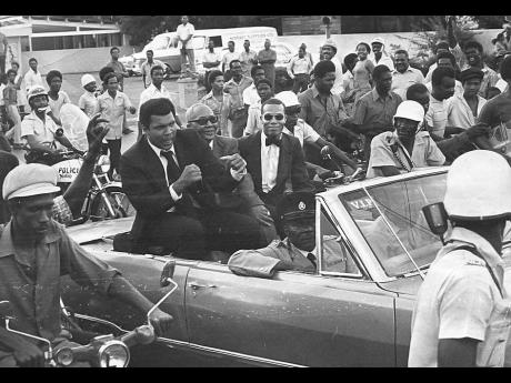 Muhammad Ali (left) responds to a request from hero-worshipping onlookers to “show us your fists”, during the 22-car motorcade from the Norman Manley International Airport on December 28, to The Jamaica Pegasus hotel shortly after the champion and his 