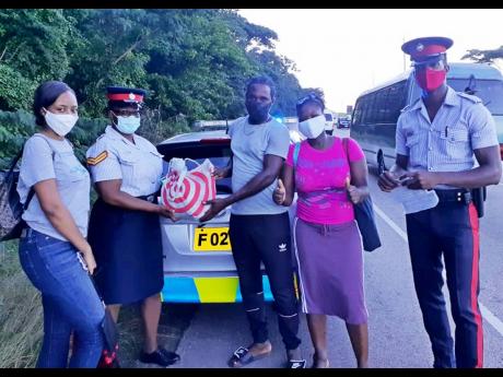 Police officers Leteacher Ennis (second left) and Teran Spence (right), of the St Ann police Community Safety and Security branch, present a gift package to a lucky motorist and his relatives.   