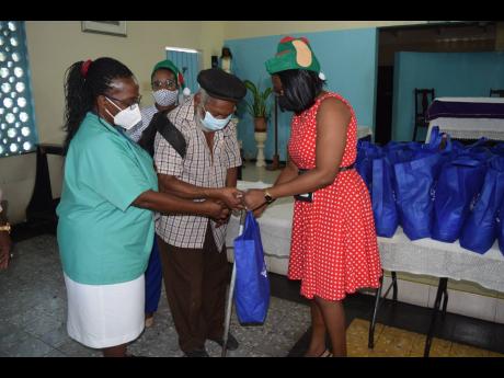Glen Stoner, senior citizen of Greenwich Town, accepts his gift package from Dionne Mason-Gordon, SAJ operations manager – property & administration,  while Nurse Deanmarie White assists and Jean Hinds, internal auditor (partly hidden), looks on. The pre