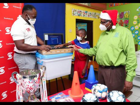 Craig Richards (left), Scotiabank May Pen branch manager, examines some of the items provided for the May Pen Primary School sports department from the funds won in the 2019 Concacaf Scotiabank Next Play football tournament. With him are principal, Major P