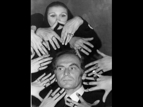 In this September 1969 file photo, French fashion designer Pierre Cardin’s face is framed by 10 hands of models like a sculptur of goddess Siva ornamented with a collection of rings designed by Cardin from his latest jewellery collection, in Paris, Franc