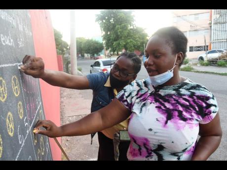Taneka McKoy Phipps and daughter Shereece Phipps, both students of The Mico University College, put the daily lesson on a wall blackboard in Tavares Gardens, southwest St Andrew. 