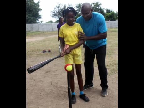Uel Gordon (right), President of the Jamaica Baseball Association,  demonstrates the proper batting technique to a young participant, during a baseball seminar at Gregory Park Primary School in Portmore, St Catherine in 2014.