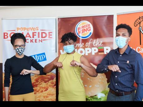 Arlene Martin (left), Acting General Manager, Professional Football Jamaica, touches elbows with Sabrena McDonald Radcliffe, Head of Sales and Marketing at Restaurant Associates Limited (RAL), while Oshane Thoms, Brand Manager, Popeyes and Little Caesars P