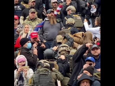 In this January 6 image from video provided by Robyn Stevens Brody, a line of men wearing helmets and olive drab body armor walk up the marble stairs outside the US Capitol in Washington in an orderly single-file line, each man holding the jacket collar of