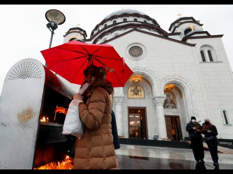 A woman lights candles during the Orthodox Christmas Eve, in front of St Sava temple, in Belgrade, Serbia, Wednesday, January 6, 2021. Orthodox believers in Serbia celebrate Christmas on January 7, according to the Julian calendar.