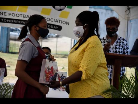 
Elaine Walker-Brown, president of St Catherine Football Association, hands over a table to Daina Wright, a female footballer and student of Spanish Town High School, during a tablet donation ceremony at Spanish Town Prison Oval on Friday.
