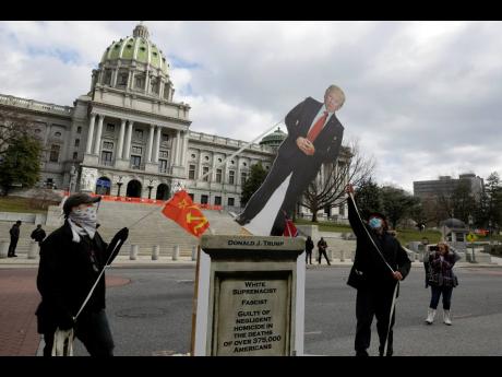 Political activists pull down a cut-out of President Donald Trump while staging a demonstration in front of the Pennsylvania State Capitol in Harrisburg, Pennsylvania, on Sunday.