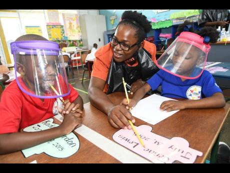 Teacher Taneka McKoy-Phipps, who gained popularity for her walkabout blackboard campaign, explains a concept to Kador Gordon (left) while Jenae Lewis listens attentively at Union Gardens Infant School in Kingston 13 on Tuesday. Business mogul and philanthr