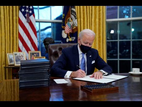 President Joe Biden signs his first executive order in the Oval Office of the White House on Wednesday, January 20, in Washington.