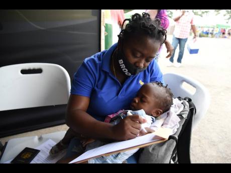 Peta-Gay Harris fills out a passport form for her daughter, Raine-Alexis, during a visit by the mobile unit of the Passport, Immigration, and Citizenship Agency in Spanish Town, St Catherine, on Saturday.