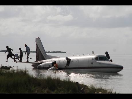 Residents of Rocky Point, Clarendon, scavenge for souvenirs from the plane that crash-landed along the coastline on Saturday evening.