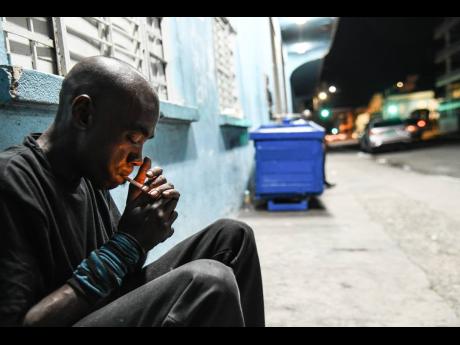Lionel Johnson, 47, lights a cigarette while sitting outside the Kingston and St Andrew Municipal Corporation temporary night shelter on Church Street. Deported from New York almost two decades ago, Johnson said he has no relatives here in Jamaica. He said
