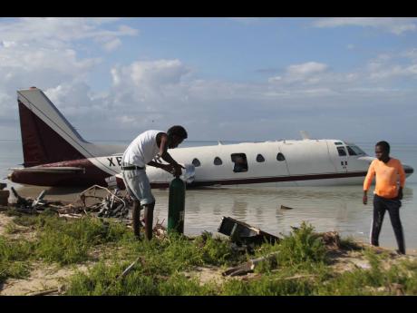 Residents of Rocky Point, Clarendon, scavenge for equipment and paraphernalia from a plane that crash-landed on Saturday, January 23.