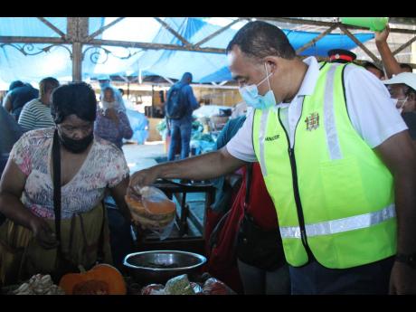 Minister of Health and Wellness Dr Christopher Tufton purchases pumpkin from Shirley Lewis, a vendor in the Mandeville Market, during coronavirus sensitisation activities on Wednesday. 