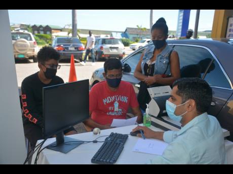 Ramkumar Junagadala (centre), his son Jayden and wife Viviene (standing) are served by an Indian consular officer during a pop-up camp by the Indian High Commission in Montego Bay, St James, last weekend.
