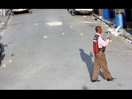 In this 2008 file photo. a policeman walks across 28 spent shell markers on Laws Street in downtown Kingston after a daring attack by gunmen in which 13 persons were injured. One person later died. The shooting was believed to be a result of a fued between