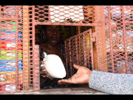 A shopkeeper in Kingston hands a bag of flour weighing two pounds to a customer on Tuesday. Jamaica Flour Mills, the main wholesaler of flour in the island, has increased prices by up to 14 per cent. 