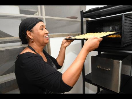 Hapi Crunch CEO Sharon Tucker places a try of thinly sliced bananas into the drier for processing at her Linstone Crescent, St Andrew, business last Friday.