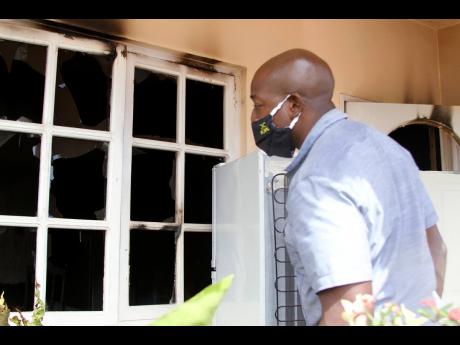 Nathaniel Stewart/Photographer 
Clarendon South Eastern Member of Parliament Pearnel Charles Jr examines the damage done to this home, which was firebombed in Lionel Town on Friday night. It is the third house in the community to be firebomded in two weeks