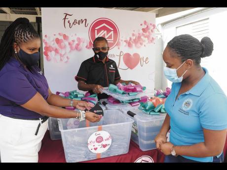 Victoria Mutual Group President Courtney Campbell (centre) looks on while Clover Moore (left) shows Hotiyana Brown, secretary to the Inspector of Poor, some of the masks that were also donated to the shelter.
