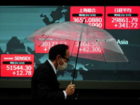 A man, wearing a protective face mask to help curb the spread of the coronavirus, walks in the rain past an electronic stock board showing Japan’s Nikkei 225 and other Asian indexes at a securities firm on Monday, February 15, in Tokyo. Asian shares star