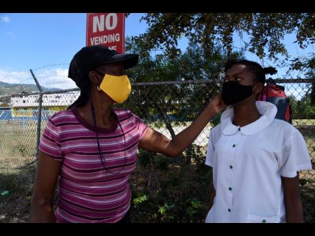 Beverly Smith fixes her daughter Brianna Jackson’s mask as they await transportation outside Mona Heights Primary School yesterday.