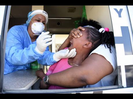 Dr Shanice Mullings (left) prepares to swab the nostrils of eight-year-old Actavia Harging, who was scared of submitting to the coronavirus test in Central Village, St Catherine, on January 13. The Government is hoping to vaccinate at least two million Jam