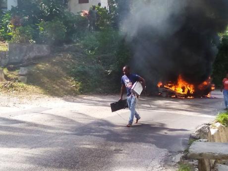 The driver of a Toyota motor car walks away with musical equipment he salvaged from the vehicle, which burst into flames on the Long Hill main road in St James on Sunday.