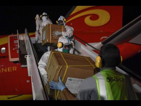 In this March 30, 2020 photo, Venezuelan workers, wearing protective gear as a preventive measure against the spread of the new coronavirus, unload humanitarian aid from China at the Simon Bolivar International Airport in La Guaira, Venezuela.