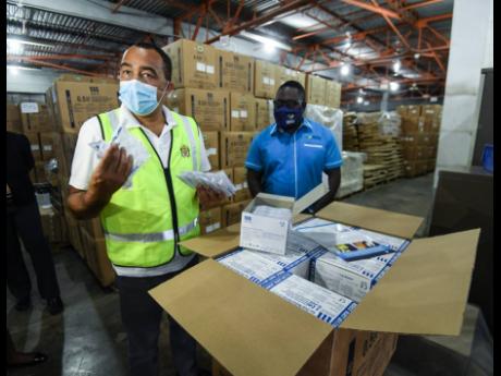 Health and Wellness Minister Dr Christopher Tufton examines syringes for Jamaica’s vaccination programme while Dwayne Linton, storage manager at the Shalimar storage facility, looks on. The minister was conducting site visits in Vineyard Town and on Marc