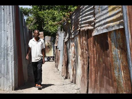 Delroy Young walks along a zinc-fenced pathway in Naggo Head, Portmore. Residents are hopeful that the blighted community can be transformed through significant real-estate investment.