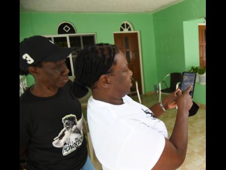 Vinnette Robb Oddman, sister of Bunny Wailer, looks at photos of the late musician on a cell phone at the family home in Nine Miles, St Ann, on Tuesday. Behind her is another sister, Monica Robb.