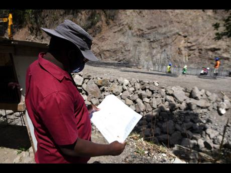 Project Manager Orville Clarke looks over the blueprint as work progresses on the rehabilitation of a breakaway along the Gordon Town main road in St Andrew. The road was damaged during heavy rains last November and is now impassable to vehicular traffic.