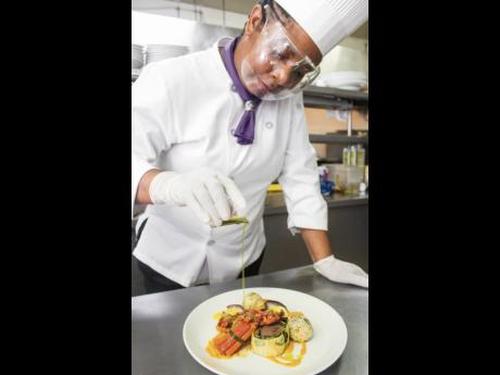 Chef Patrice Malcolm adds the final drizzle to her Beef Wellington, encased in callaloo and served with a jerk Hollandaise sauce, sautéed herb butter lobster, sticky rice stuffed with crab, pumpkin purée and seasonal vegetables.