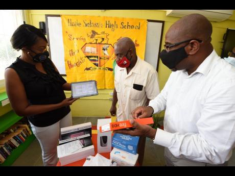 Haile Selassie High School Principal Lorenzo Ellis (centre) sorts through some of the tablets, face masks, soap dispensers and hand sanitisers donated to the institution yesterday with past students Georgina Henry-Smith and Milton Morrison yesterday. The d