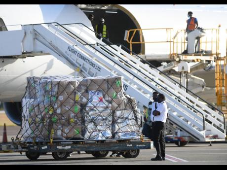 Two pilots stand next to the shipment of vaccines shortly after they were offloaded at the Norman Manley International Airport yesterday.