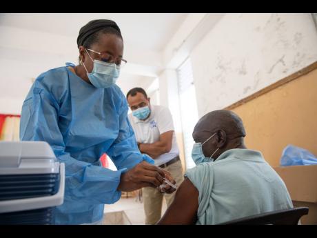 Public health nurse Kathy-Ann Bryan administers a dose of the Oxford-AstraZeneca vaccine to Bridge Barker, a 75-year-old senior citizen, at The Golden Age Home in Kingston on Tuesday. Looking on is Minister of Health and Wellness Dr Christopher Tufton.