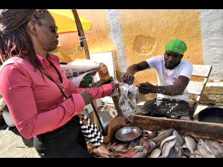 Agustus Fowler handing over fish to customer Charmaine King at the Princess Market in Spanish Town. 
