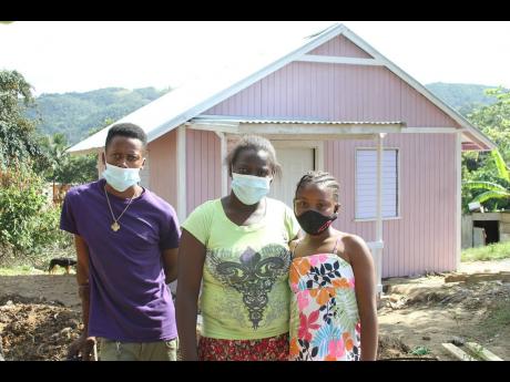 Evadney Johnson (centre) with Charlette Thomas and Davil Johnson, two of her five children, in front their house built by Food For The Poor in partnership with reggae artiste Tanya Stephens and BOOM Energy Drink. Ms Johnson’s new home is the fifth of 10 