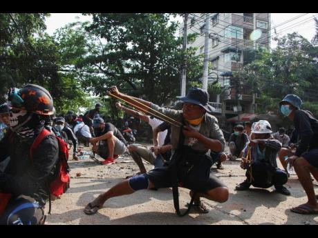 Anti-coup protesters use sling shot to confront police at Thaketa Township in Yangon, Myanmar on Sunday.
