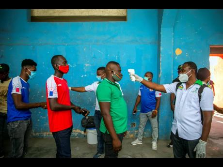 Health ministry workers check the temperature of mask-wearing fans as a precaution against the spread of the new coronavirus, before entering the stadium prior to the start of the Concacaf World Cup-qualifying soccer match between Haiti and Belize in Port-