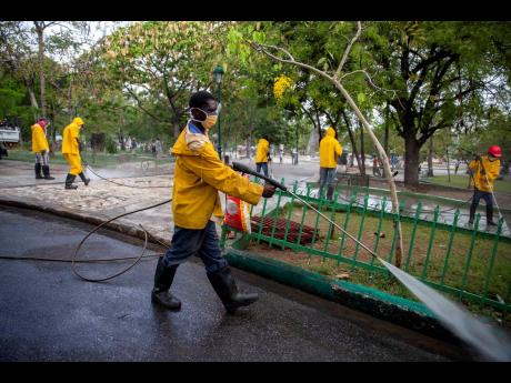 In this April 7, 2020 file photo, city hall workers spray disinfectant in the street and a park in Petion-Ville, Haiti.