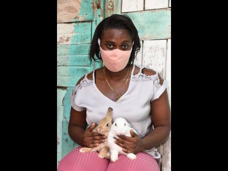 Young mother,  Gewana Reid, holds two of the rabbits she raises and sells in Denham Town, Kingston.