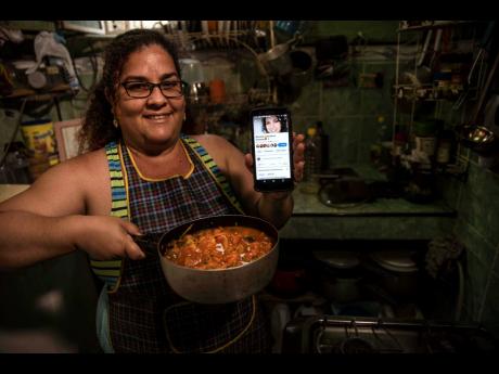 
Contributor Yuliet Colon poses for a photo holding a pot of her creation, ‘Cuban-style pisto manchego’,  and her phone that displays the Facebook page, ‘Recipes from the Heart’, in her home in Havana, Cuba, on Friday, April 2. 