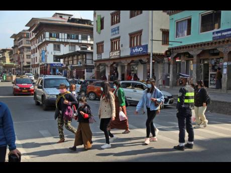 Bhutanese people wearing face masks as precaution against coronavirus cross a street in Thimpu, Bhutan, yesterday. The tiny Himalayan kingdom, wedged between India and China, has vaccinated nearly 93 per cent of its adult population since March 27. Overall