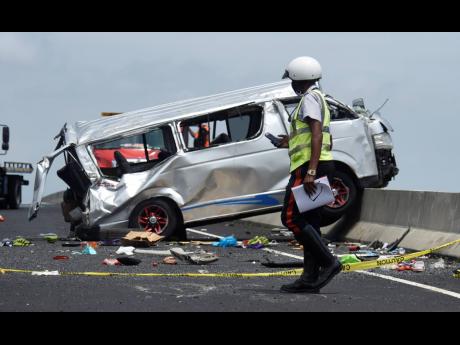 A policeman walks by the Toyota Hiace minibus that was involved in a crash on Highway 2000 on Monday.  Five people were killed in the collision.