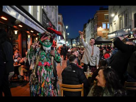 People sit at set-up tables outside pubs in Soho, in London, on the day some of England’s third coronavirus lockdown restrictions were eased by the British government on Monday. Pubs, shops and hairdressers have opened as lockdown restrictions are eased 